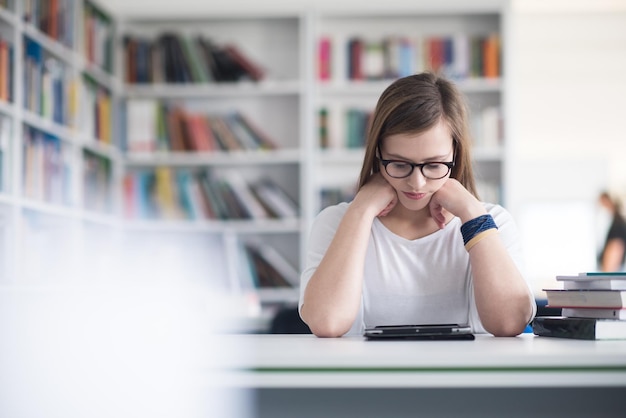 étudiante étudiant à la bibliothèque de l'école en utilisant une tablette et à la recherche d'informations sur Internet