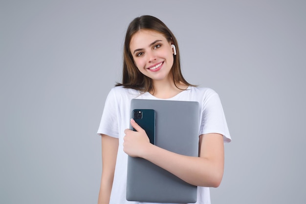 Une étudiante heureuse, une jeune femme, une étudiante en T-shirt blanc tenant un ordinateur portable isolé sur le gris.