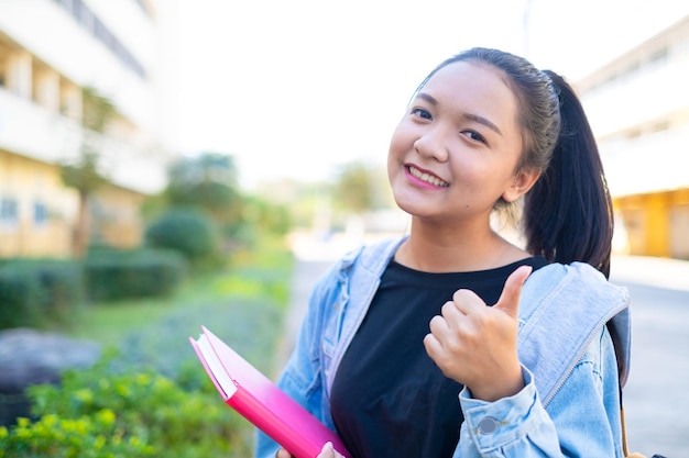 Une étudiante heureuse tient un livre et un sac à dos à l'école