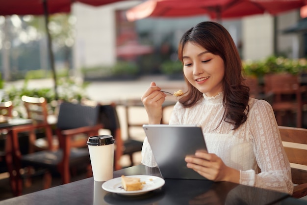 Une étudiante heureuse travaille sur une tablette numérique et se détend dans un café