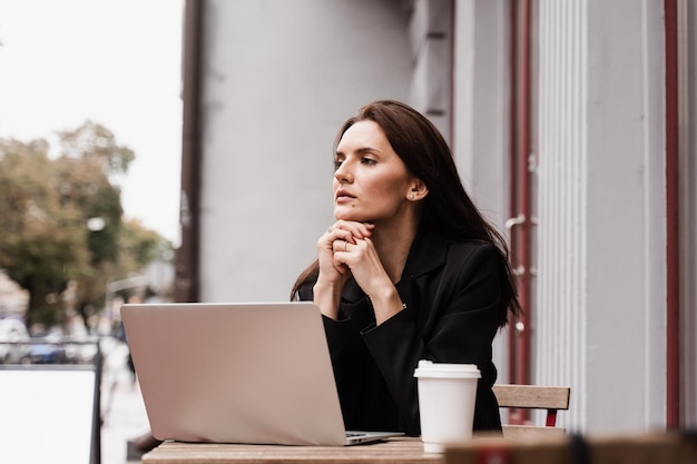 Une étudiante intelligente avec un ordinateur portable et une tasse de café étudie l'anglais en ligne à l'école linguistique en plein air du café Une jeune femme séduisante a une leçon de communication vidéo avec l'enseignant