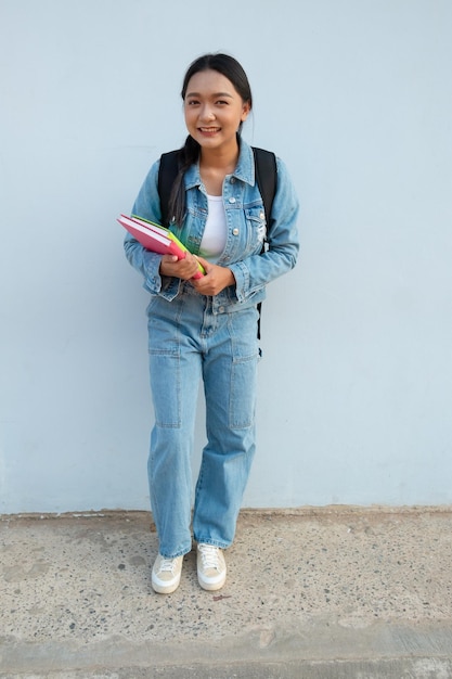 Étudiante jeune fille debout à l'école porter jean tenir livre avec sac à dos fond bleu