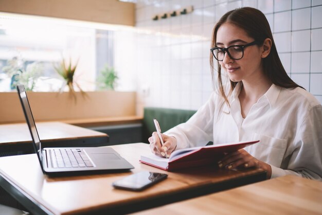 étudiante à lunettes profitant du temps sur le campus universitaire tout en notant des choses drôles de la journée