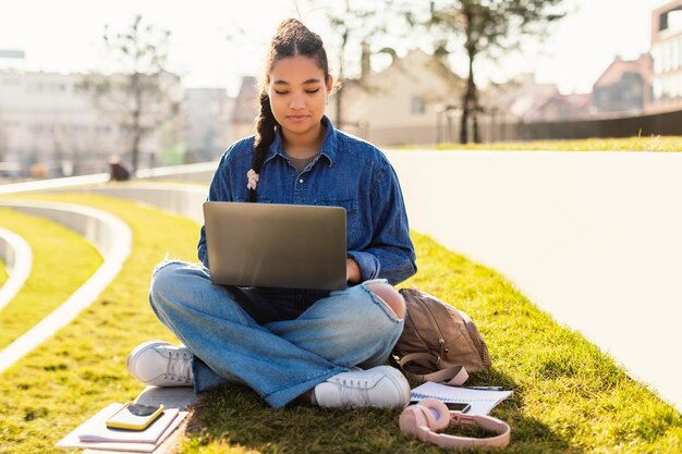 Étudiante métisse assise avec un ordinateur portable dans le parc apprenant en ligne ayant un enseignement virtuel