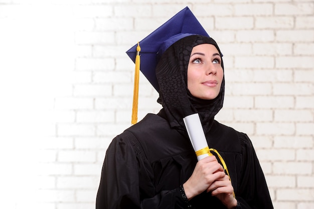 Une étudiante musulmane diplômée heureuse pose avec un diplôme à l'intérieur