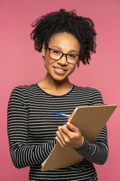 Photo une étudiante porte des lunettes et tient un dossier en souriant en regardant la caméra.