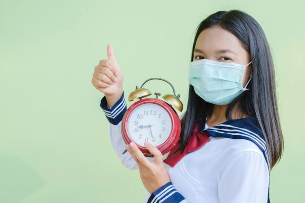 Une étudiante porte un masque avec une horloge alam, une fille asiatique, un fond vert.