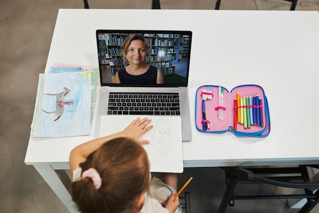 Photo une étudiante qui fait un cours vidéo à distance avec son professeur sur un ordinateur portable assise à un bureau dans la salle de classe