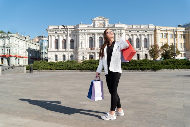Une étudiante se promène dans la ville avec des sacs à provisions et profite d'une journée ensoleillée