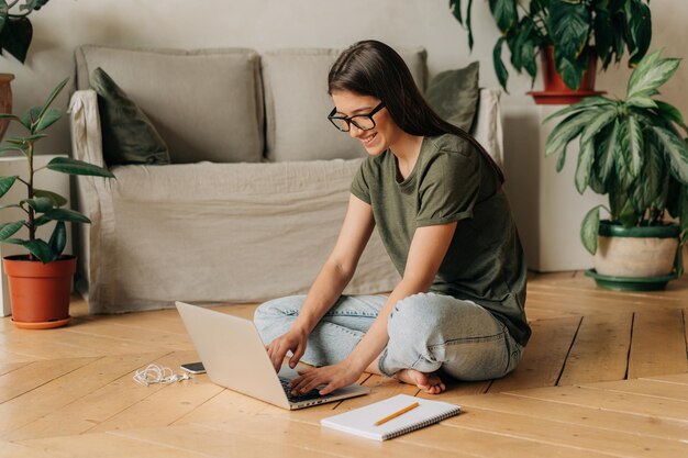 Photo une étudiante souriante assise par terre utilise un ordinateur portable pour l'apprentissage et le travail à distance