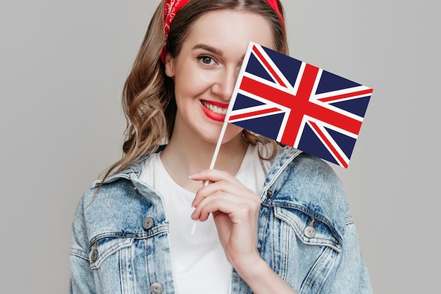 Une étudiante tient un petit drapeau britannique britannique souriant et regarde la caméra isolée sur fond gris