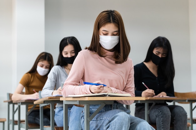 Des étudiantes adolescentes portent un masque facial et gardent leurs distances tout en étudiant en classe et sur le campus universitaire pour prévenir la pandémie de COVID-19