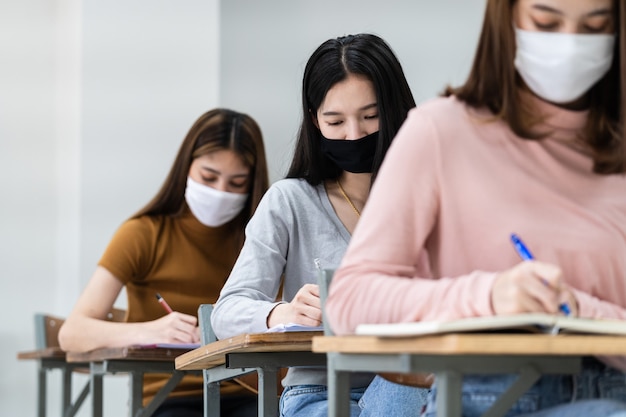 Des étudiantes adolescentes portent un masque facial et gardent leurs distances tout en étudiant en classe et sur le campus universitaire pour prévenir la pandémie de COVID-19