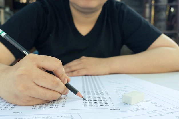 Photo les étudiantes main tenant un crayon écrivant le choix sélectionné sur les feuilles de réponses et les feuilles de questions mathématiques. les étudiants testent l'examen. examen scolaire