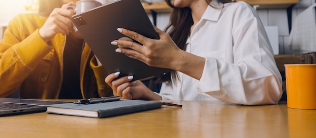 Les étudiantes notent des livres à la bibliothèque des filles asiatiques assises sur un canapé à l'aide d'un ordinateur portable et d'une tablette pour rechercher des informations en ligne dans le salon