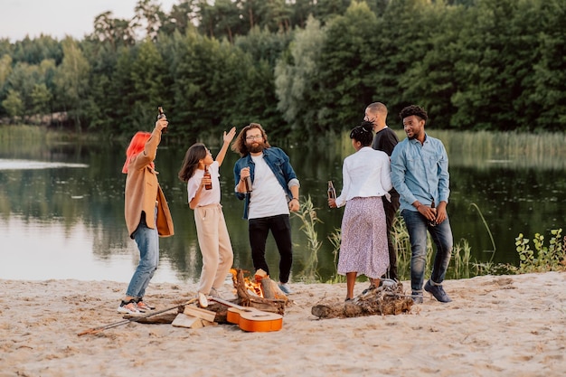 Des étudiants amis de différentes nationalités et couleurs de peau se rencontrent sur la plage au bord d'un feu de joie au bord du lac