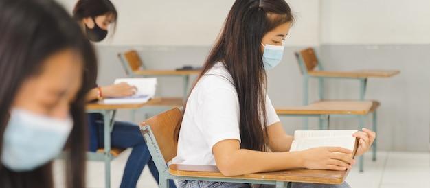 Les étudiants asiatiques de retour à l'école portent un masque facial et gardent la distance en étudiant en classe