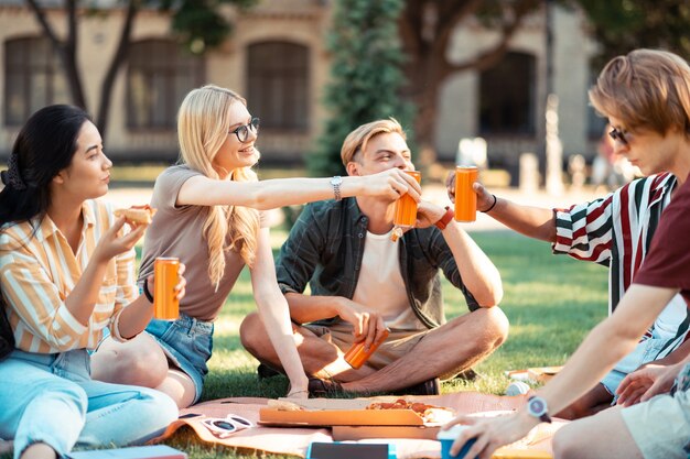 étudiants assis ensemble sur la pelouse, boire du jus et manger de la pizza