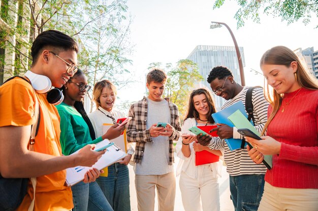 Des étudiants divers se rassemblent à l'extérieur sur le campus universitaire en souriant tout en utilisant des téléphones portables et