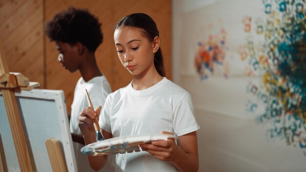 Photo des étudiants multiculturels peignent ensemble la toile dans l'édification de la leçon d'art