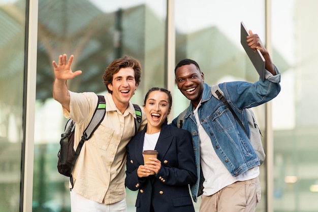 Des étudiants multiraciaux heureux agitant la main à la caméra et souriants