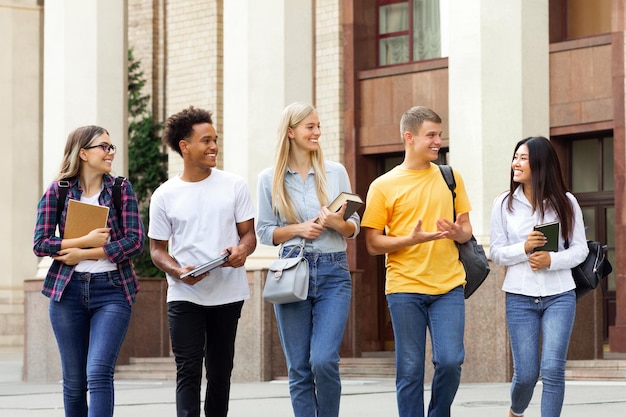 Des étudiants multiraciaux marchent contre le bâtiment de l'université pendant la pause et communiquent le panorama
