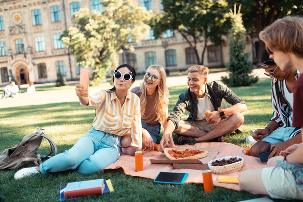 Les étudiants portant de grandes lunettes prenant des selfies assis sur la pelouse