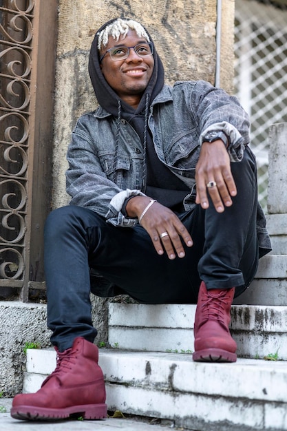 Les étudiants portent des vêtements de mode élégants, un homme afro-américain souriant avec des dreadlocks est assis sur les marches