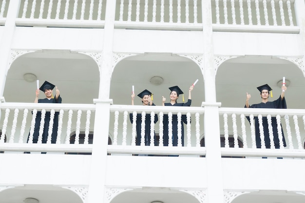 Les étudiants se sentant heureux avec les robes de graduation se tiennent au bâtiment du couloir.