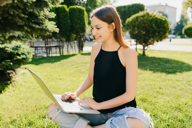 Étudier Le Concept. Belle Fille Souriante Travaillant Sur Son Ordinateur Portable, Assis Sur L'herbe Dans Le Parc.