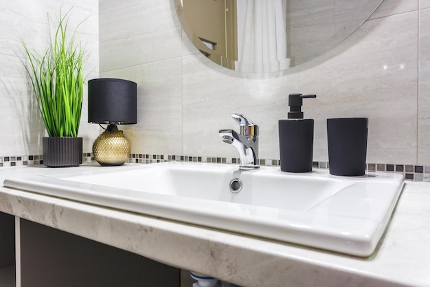 Photo Évier de robinet d'eau en céramique avec robinet avec distributeurs de savon noir et de shampoing dans une salle de bains chère