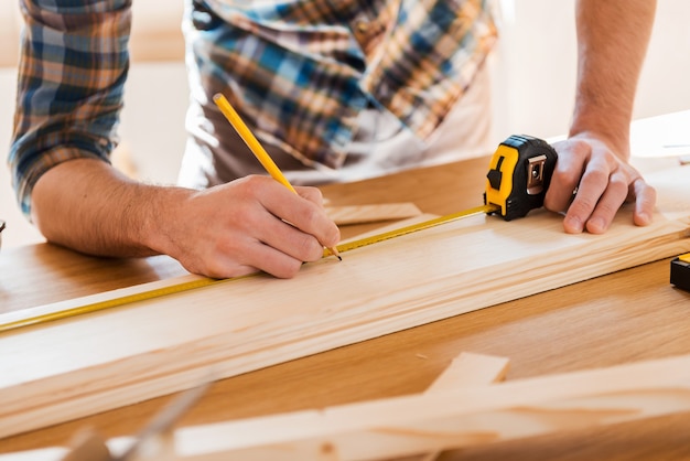 Exactement mesuré. Close-up of young male carpenter faisant des mesures sur la planche de bois