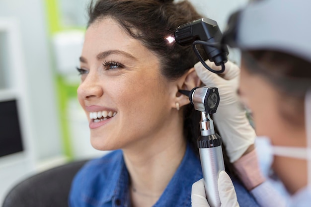 Photo examen auditif médecin oto-rhino-laryngologiste vérifiant l'oreille de la femme à l'aide d'un otoscope ou d'un auriscope à la clinique médicale