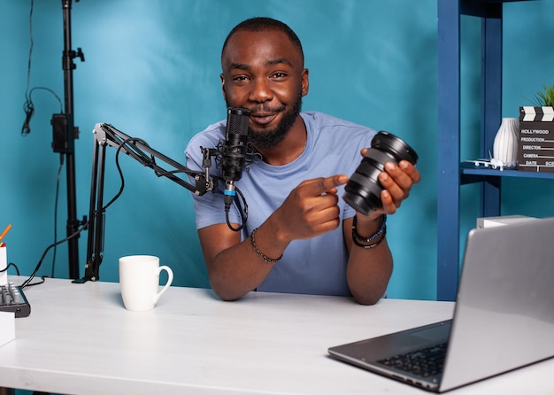 Examen du podcast d'enregistrement de Vlogger pour l'objectif zoom dslr soulignant les avantages de parler dans le microphone de studio. Influenceur parlant d'équipement de photographie assis à son bureau avec une configuration de podcasting.