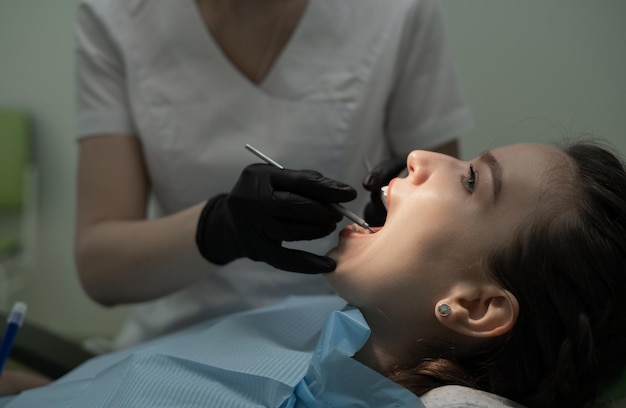 Examen en gros plan de la cavité buccale du patient par le dentiste dans des gants médicaux noirs avec des outils Traitement dentaire et prothèses dans une clinique dentaire