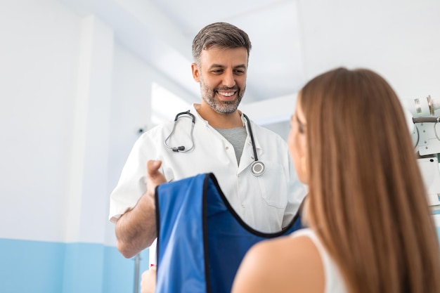 Examen radiographique patient en clinique Médecin donnant des vêtements de protection bleus au patient devant la radiographie