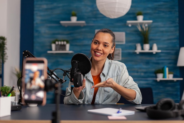 Examen de souris d'enregistrement d'influenceur souriant avec smartphone. Créateur de contenu en home studio avec microphone et téléphone portable faisant des recommandations de produits. Podcast Vlog pour les réseaux sociaux.