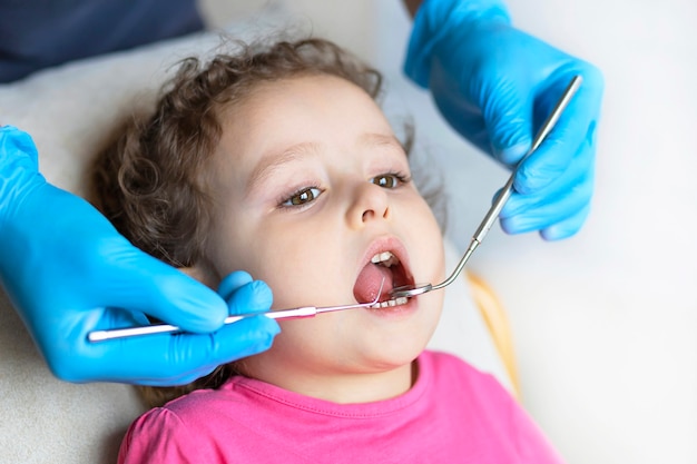 Examen, traitement des dents des enfants. examen médical de la cavité buccale avec des instruments. mains dentaires, enfant au bureau. Jolie fille souriante stomatologie. enfant en chaise de dentiste.