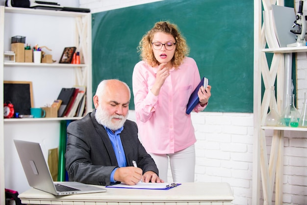 Examens Étudier avec les technologies modernes étudiant et tuteur avec ordinateur portable étudiant fille avec tuteur homme au tableau noir enseignant senior et femme à l'école leçon passe examen salle des professeurs