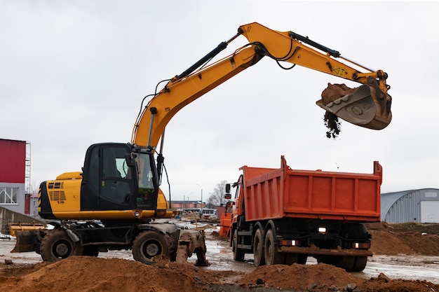 Une excavatrice charge de la terre ou du sable dans un camion-benne Aménagement d'une fosse Terrassement à l'aide d'équipements de construction lourds