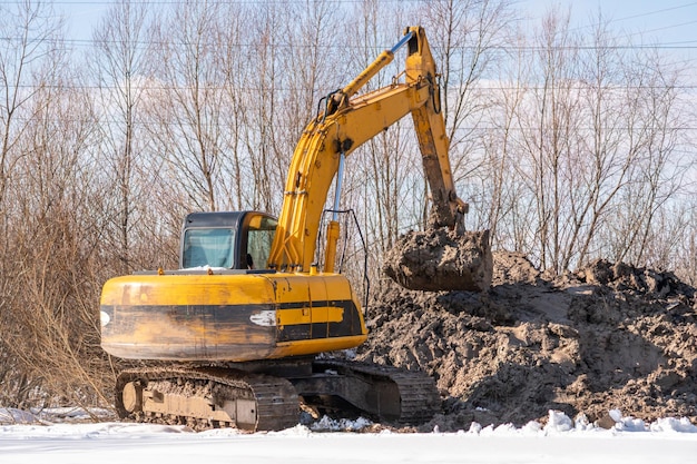 Une excavatrice jaune creuse un tas de terre.