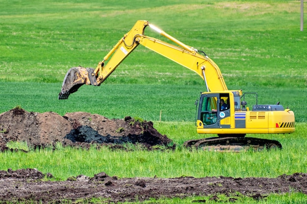 Une excavatrice jaune en train de baigner le sol dans un champ agricole