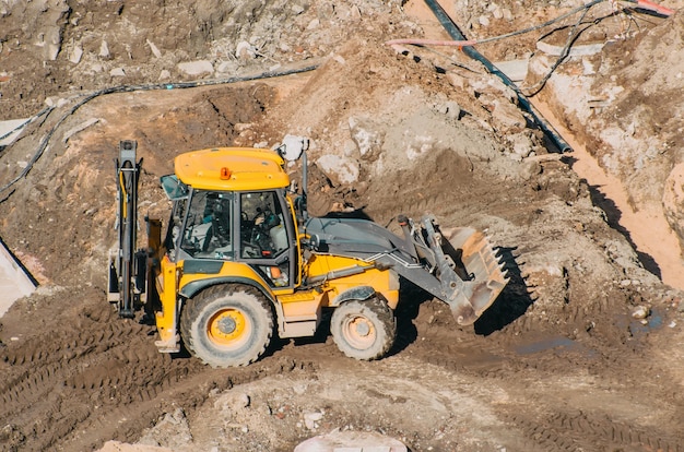 Excavatrice de tracteur avec des seaux qui traversent le cadre des terres boueuses, vue depuis la hauteur.