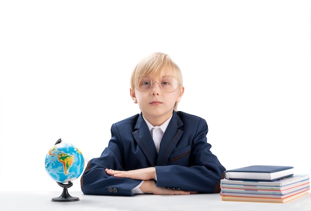 Un excellent garçon est assis à table, les mains jointes et regarde sérieusement la caméra Étudiant brillant à côté de cahiers et d'un globe