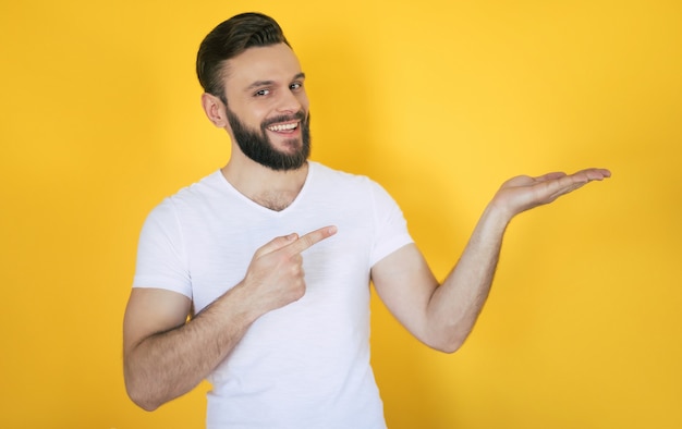 Excité Beau Jeune Homme Barbu Dans Un T-shirt Blanc Pointe Vers L'extérieur