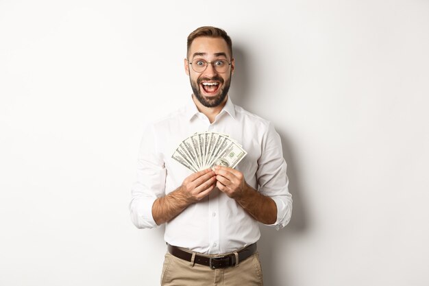 Excité bel homme tenant de l'argent, se réjouissant de gagner un prix en espèces, debout sur fond blanc