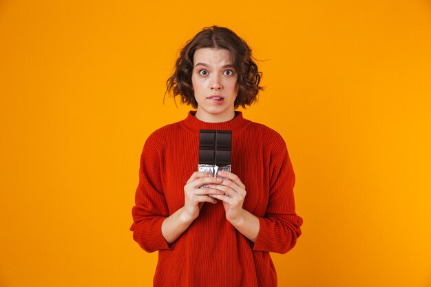 excité émotionnelle jeune jolie femme posant isolé sur mur jaune tenant le chocolat.