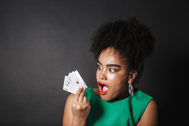 Excité femme africaine vêtue d'une robe montrant des cartes à jouer isolées sur un espace noir