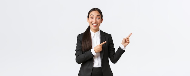 Excité femme gestionnaire asiatique vendeuse ou agent immobilier montrant une maison à vendre pointant du doigt le commerçant droit présenter un projet ou un graphique lors d'une réunion d'affaires debout en costume fond blanc