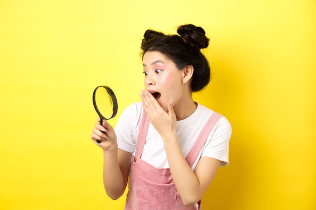 Excité fille asiatique stupide haletant se demanda, a trouvé quelque chose d'intéressant, regardant à travers la loupe, debout sur le jaune.